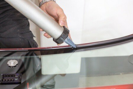 19363634 - glazier applying rubber sealing to windshield in garage tech applying glue sealing to windshield in a garage